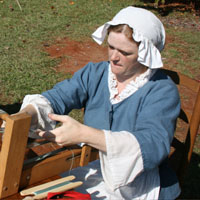 photo of a lady weaving on a loom in eighteenth century gown.